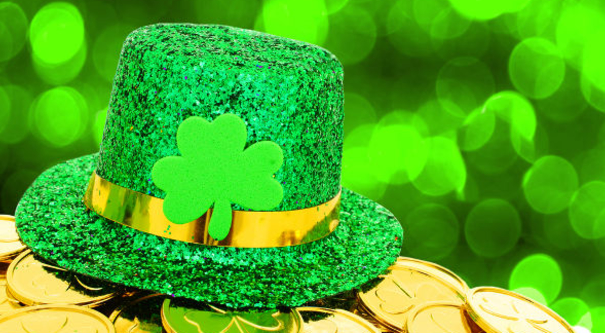 a gree glittery hat with a golden ribbon and four leaf clover in the middle sitting on a pot of golden four leaf clover coins
