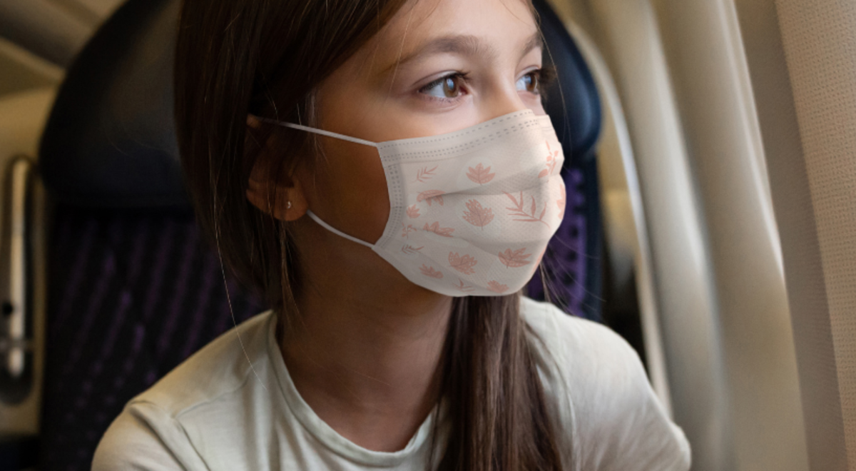 Two girls wearing a mask looking out a plane window 