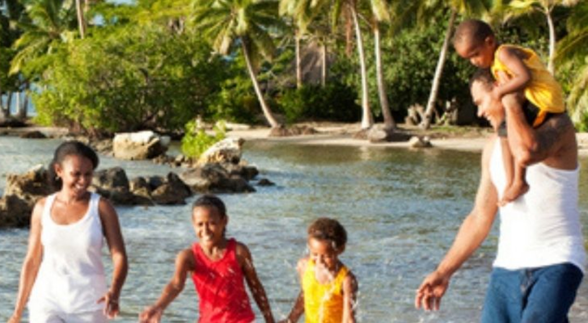 Family plays in shallow water at beach with palm tress in background