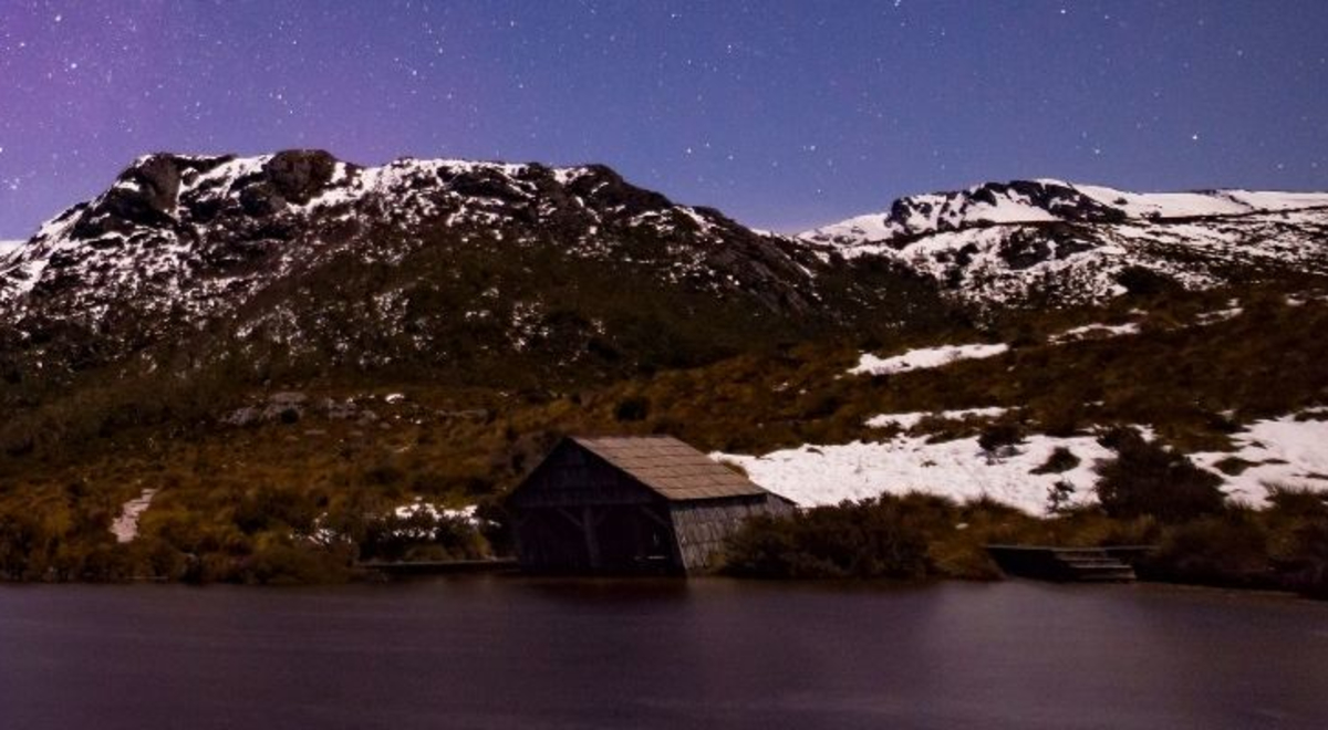 A shach in between Cradle Mountain and an aurora australis can be seen on the skies