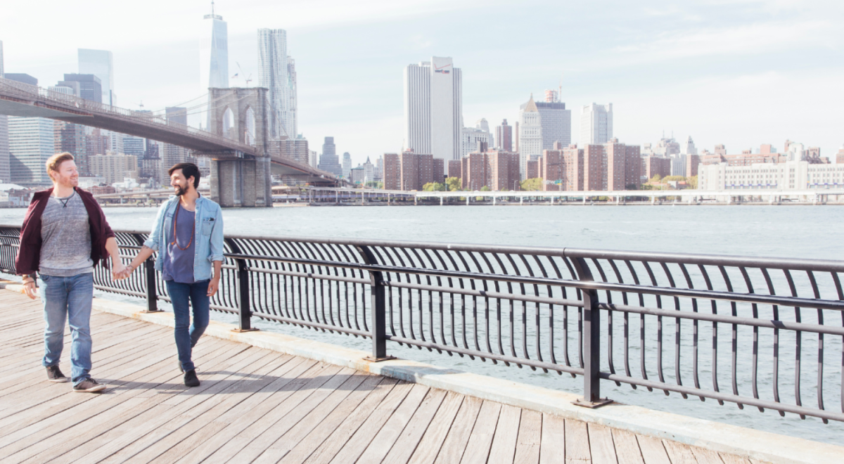 Couple walking in New York. The Brooklyn Bridge can be seen behind them.