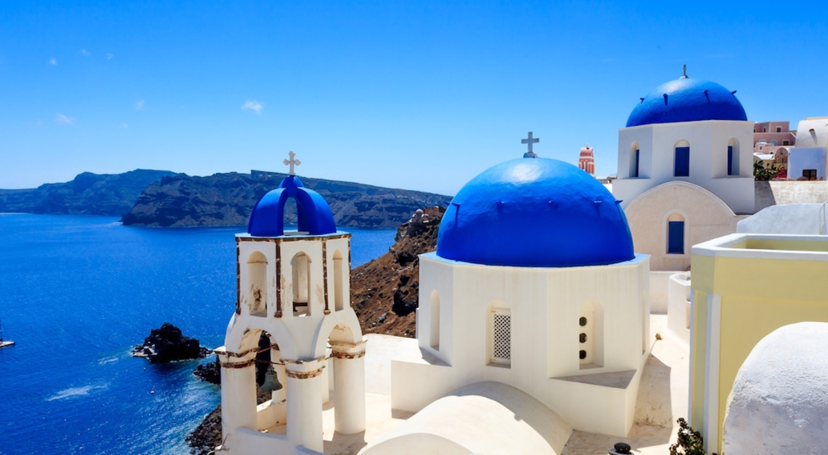 Looking over the blue domes of Santorini, Greece with a blue sea, blue sky and a large island on the horizon 