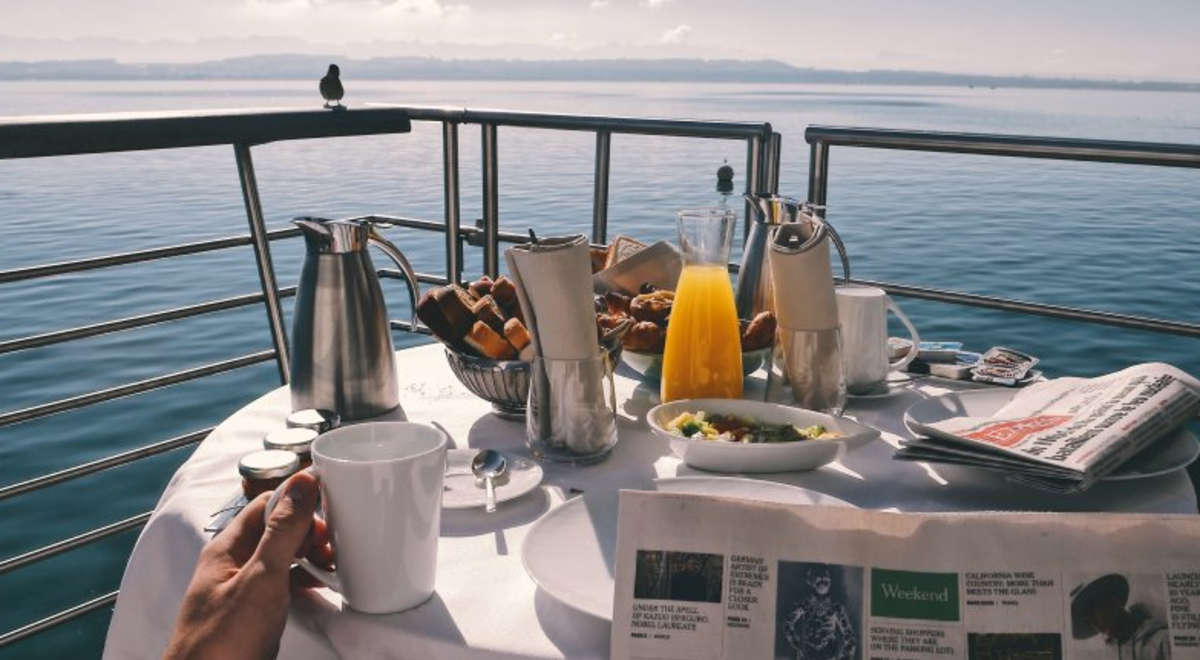 Table set for breakfast on luxury yacht with person reading newspaper in forground