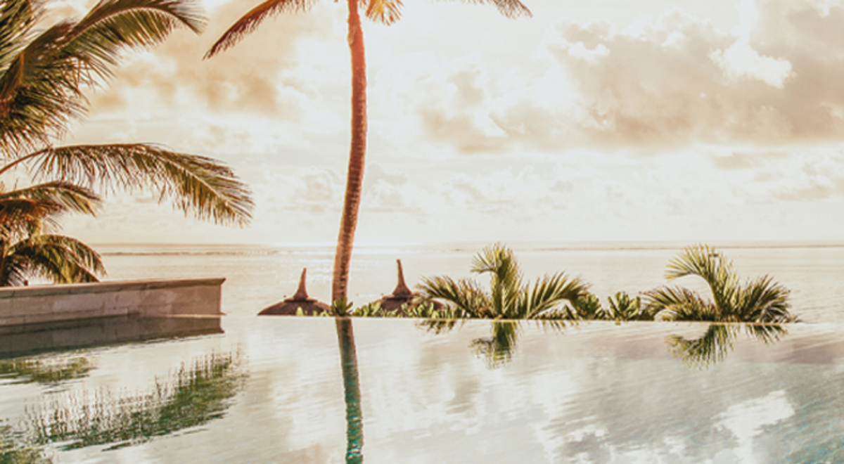 A calm sea, palms and a cloudy horizon above the edge of the still water of an infinity pool