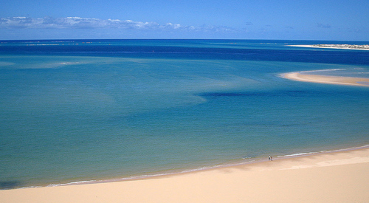 A drone's view of a large azure lagoon meeting a broad beach of golden sand 