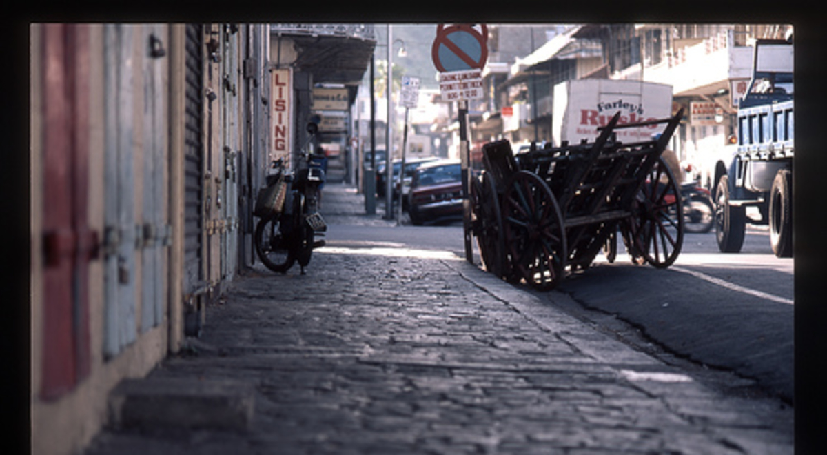 A cobble-stone footpath on a city street leads to a parked bicycle and empty wooden carts.