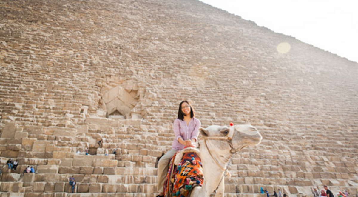 Woman riding camel in front of the pyramid 