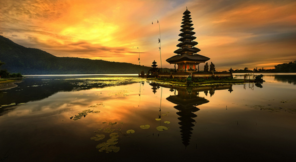 A tall oriental temple stands on an islet in the middle of a still lake at sunset