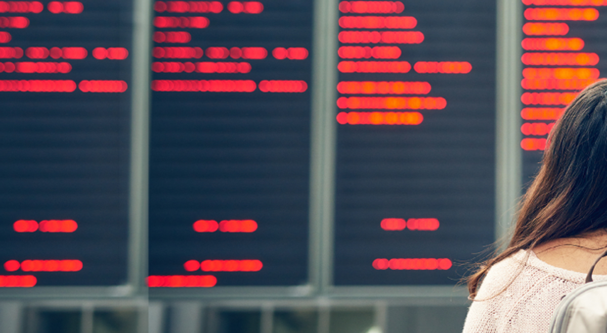 A woman traveller looks up at a digital departure board in an airport