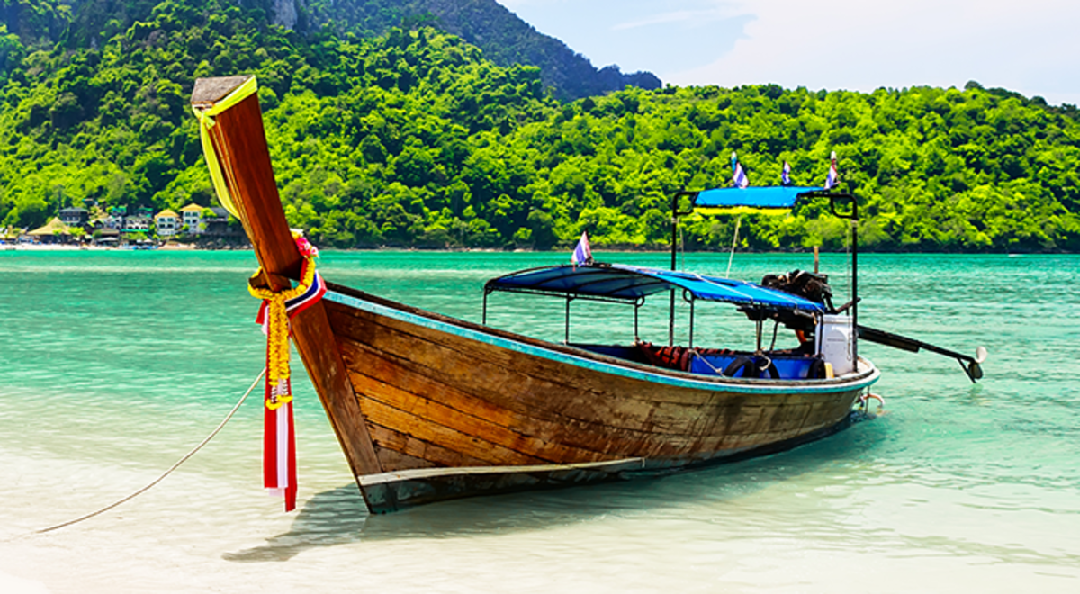 Thailand tail boat with clear water and green covered mountains 