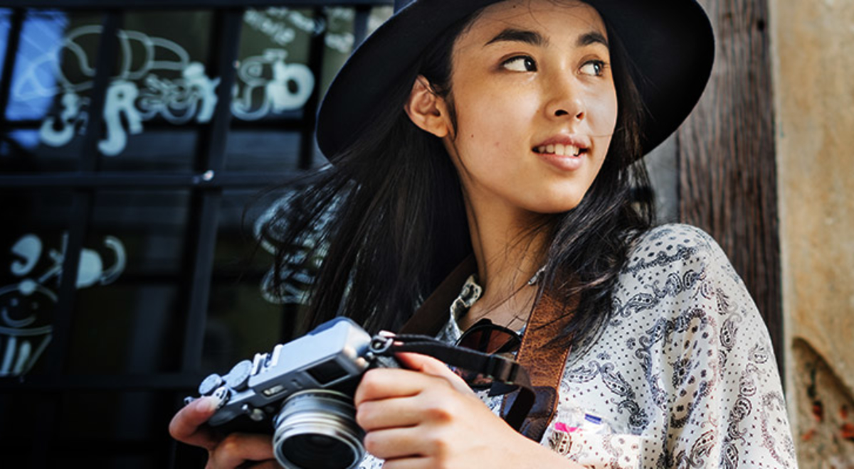 A young woman in a hat holds a camera