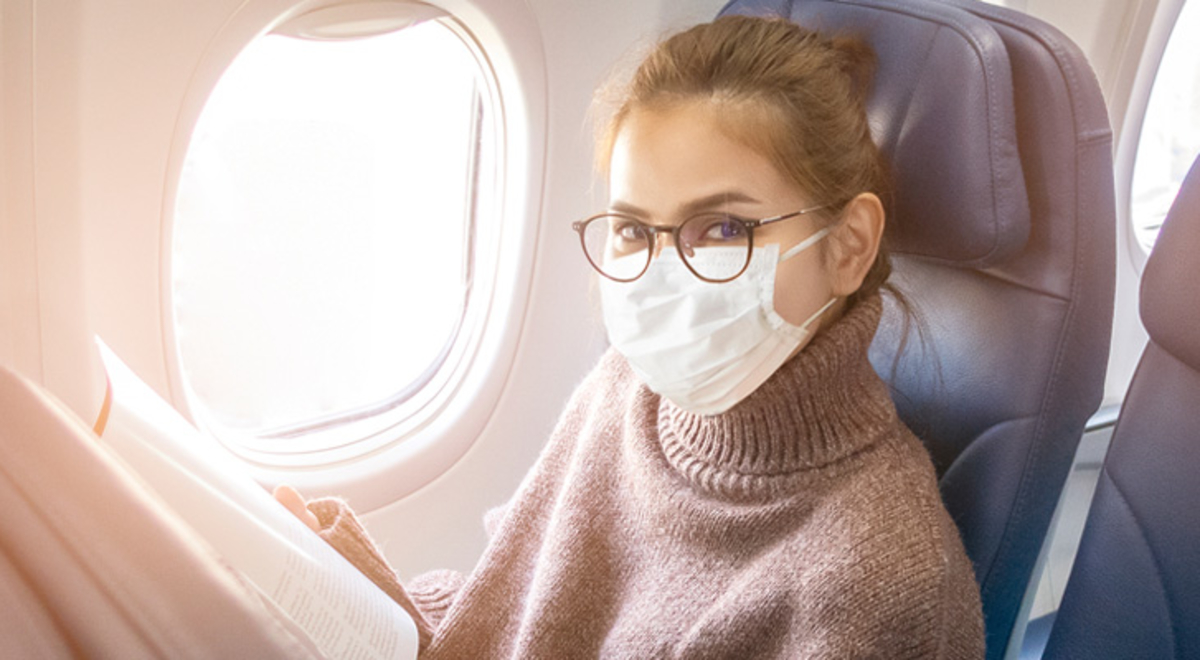 Lady sitting on a plane wearing a brown turtleneck with a mask and glasses 