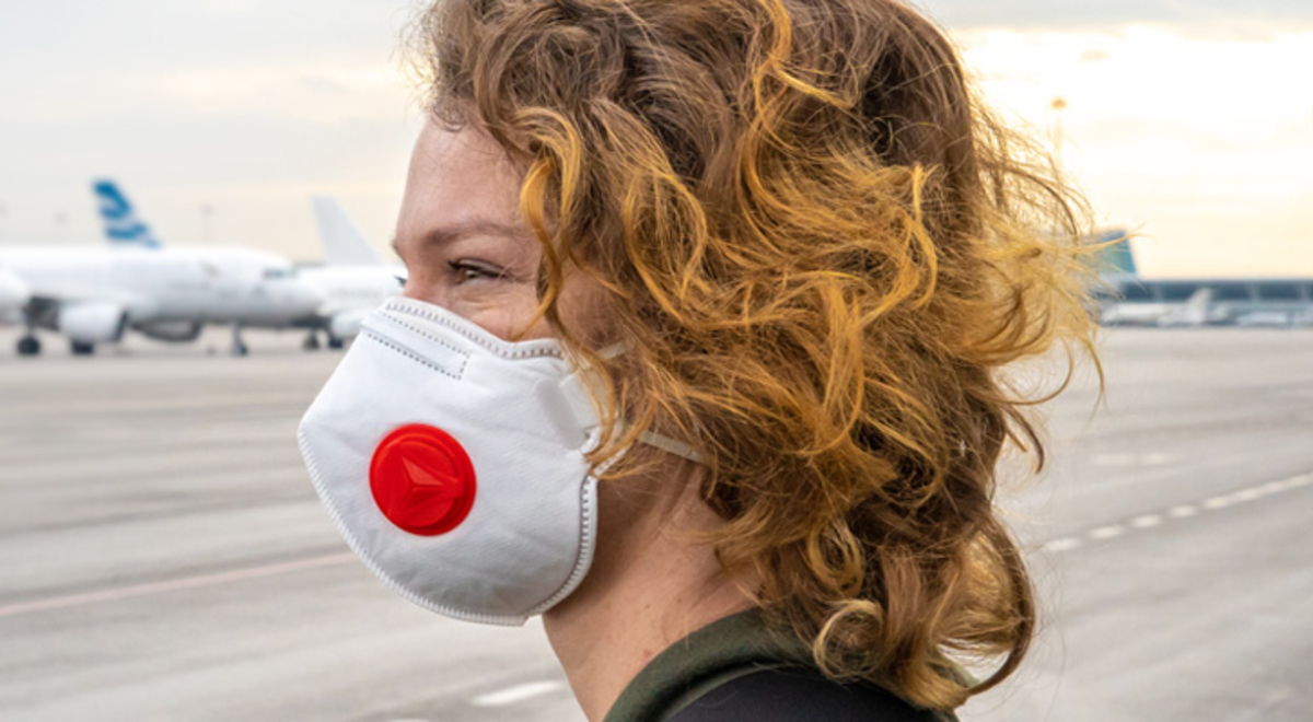 A woman in a Covid mask looks out toward a runway tarmac where passenger jets  are parked