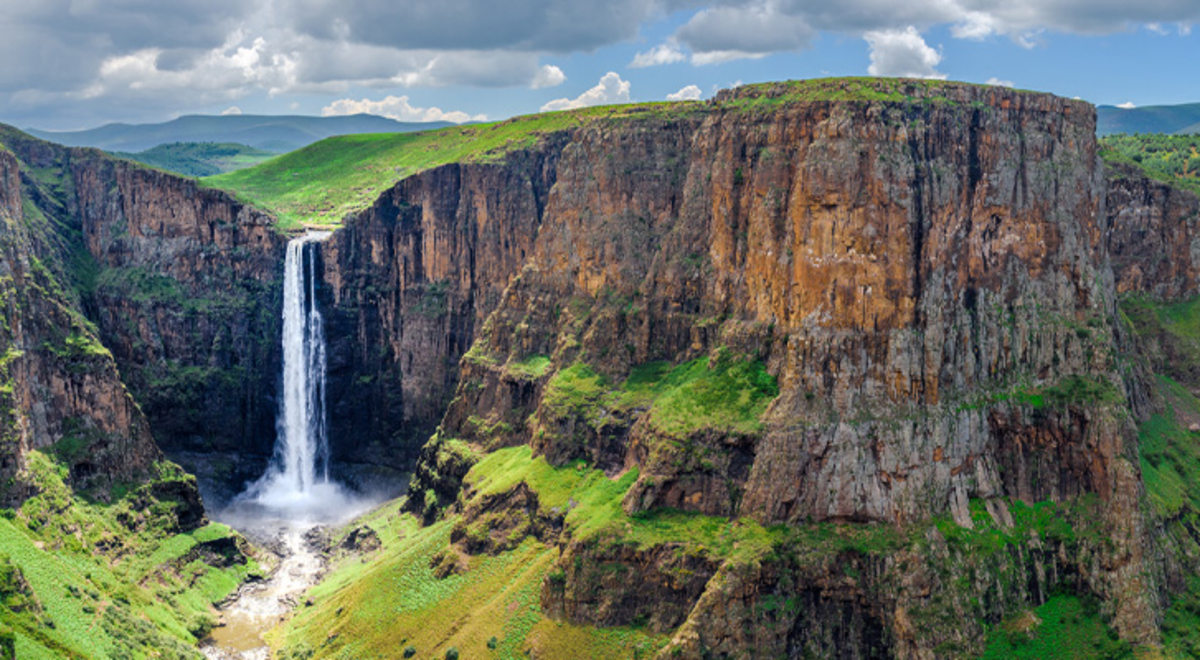 A waterfall falls from cliffs coloured green and brown in Lesotho Africa 