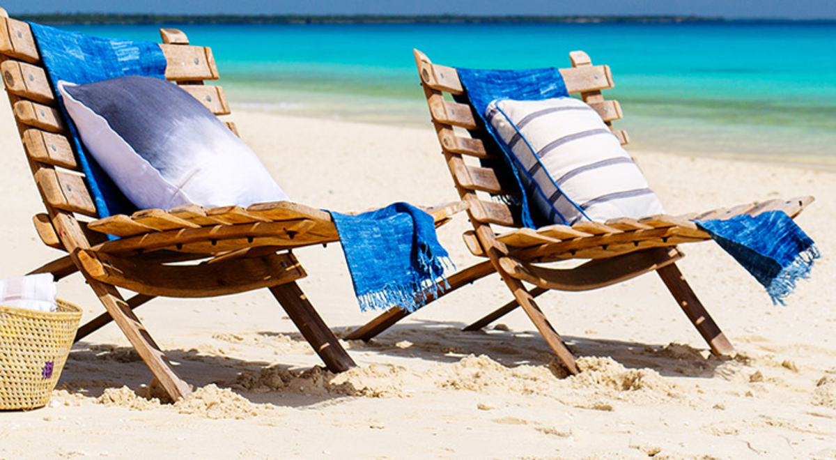 beach chairs with towels and cushions and picnic basket sitting on white sands of the beach with blue ocean in background 