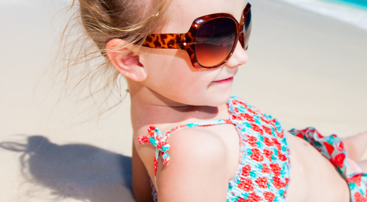 A girl in sunglasses lies on a beach looking out to sea