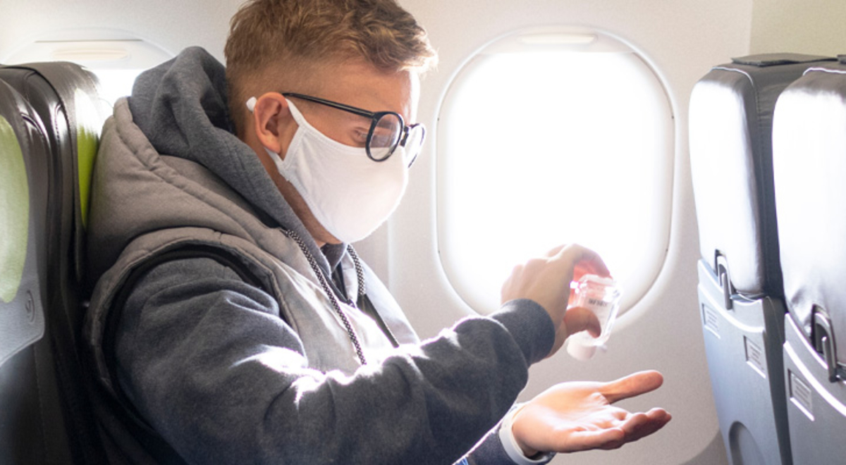 Man on a plane wearing a face mask and using hand sanitiser