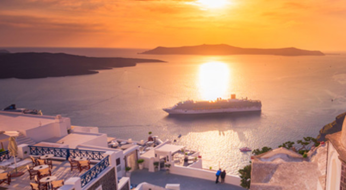 A cruise ship sails to shore in a bay below Santorini, Greece at sunset