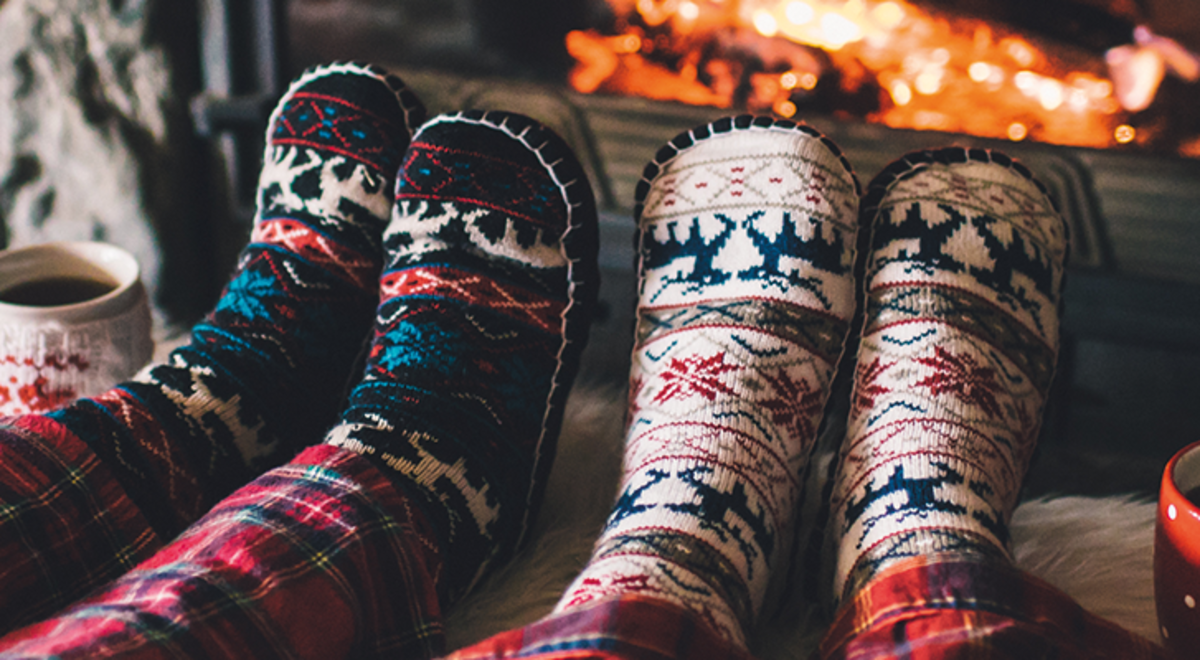 The legs of a couple in pyjamas and slippers next to coffee cups with feet up in front of a glowing fireplace