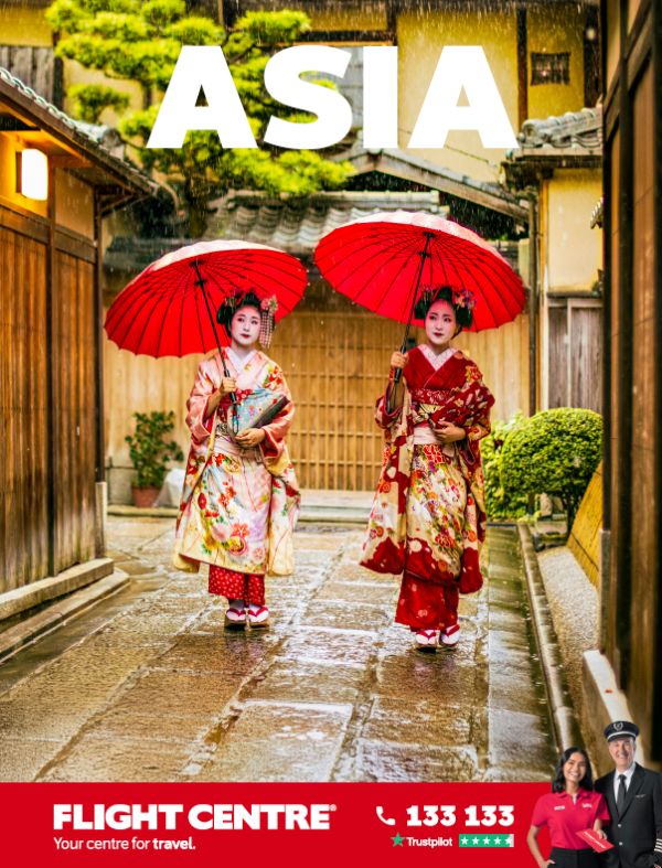 Two women in colourful kimono holding red paper umbrellas walking along a rain-soaked traditional Japanese alleyway