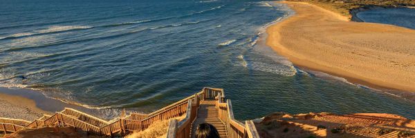 Woman walking down steep wooden steps towards a beach in the late afternoon