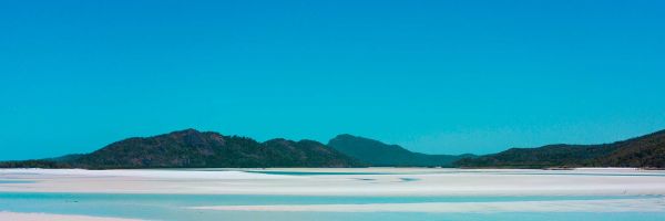 Wide shot of a woman standing ankle-deep in crystal clear blue ocean water