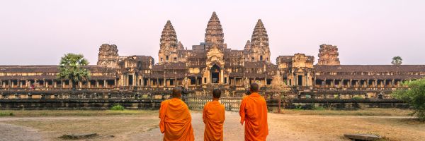 Three Buddhist monks in orange robes standing in front of Angkor Wat