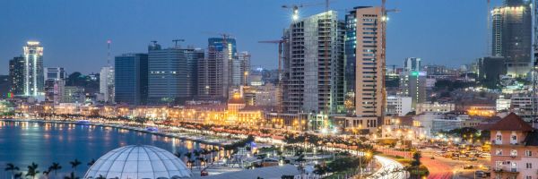 Luanda city at night - several skyscrapers topped with cranes alongside streets lined with palm trees