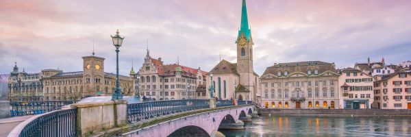 White and beige Swiss buildings along a river, with an archway bridge 