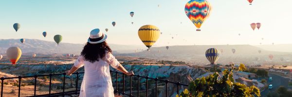 Person in white standing on a balcony looking at hot air balloons