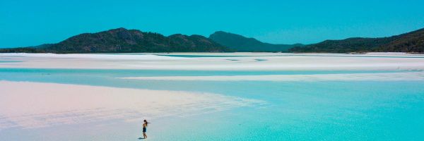 Wide shot of a woman standing ankle-deep in crystal clear blue ocean water