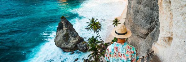 Person walking down steep, narrow rock steps towards a hidden beach cove