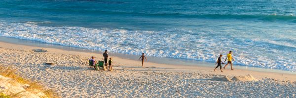 Beach with white sand under a bright sunrise with towering rocks across the ocean in the distance
