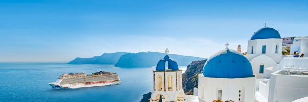 Cruise ship on a clear ocean, framed by bright white Greek buildings tipped with blue roofs