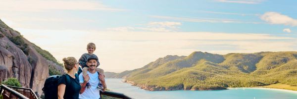 Family of 3 on a walkway overlooking blue water and tree-covered hills