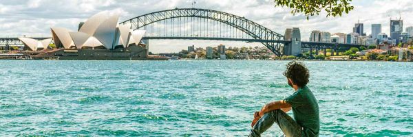 A man sitting on wall edge overlooking Sydney Harbour Bridge and the Opera House
