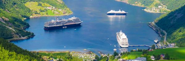 Drone shot of cruise ship in between green Norwegian landscape