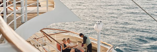 Couple on a cruise ship sitting in a round couch being served wine by a waiter in the early afternoon
