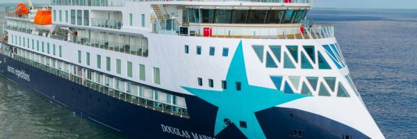  The Aurora Expeditions expedition cruise ship Douglas Mawson photographed from an elevated angle, showing its striking white and navy hull with a large teal star design on the bow, sailing on calm open water under a partly cloudy blue sky.