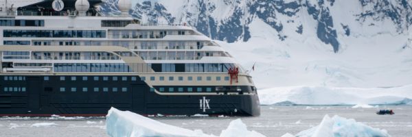 Explorers in inflatable boats sailing through icy water with a Hurtigruten cruise ship and glaciers in the background