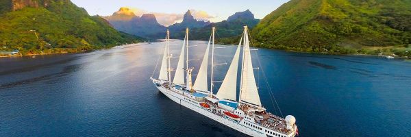 Cruise ship with sails in a bay surrounded by lush green mountains