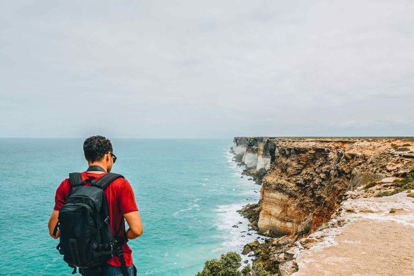Backpacker standing on the edge of a sandy cliff looking at the waves