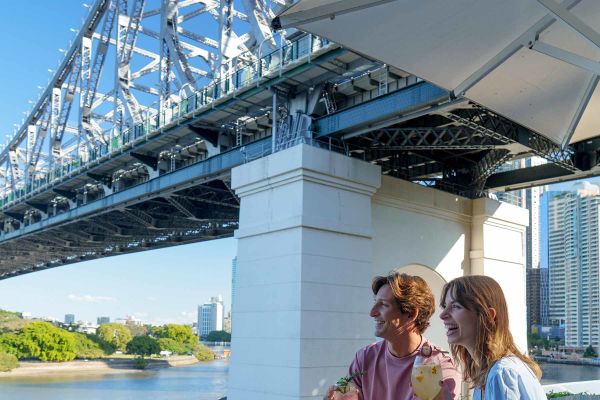 Young couple drinking cocktails sitting under Sydney Harbour Bridge