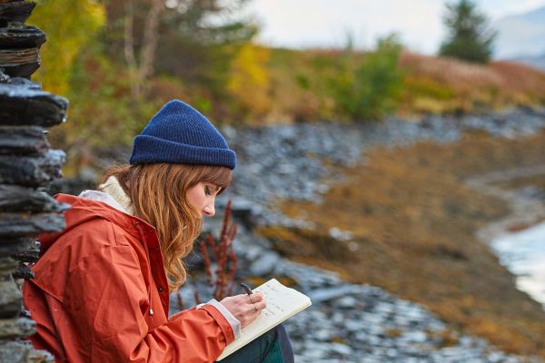 Lady journalling while sitting on rock along water