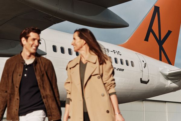 Couple wearing brown jackets walking across the tarmac with an Abercrombie & Kent aeroplane in the background