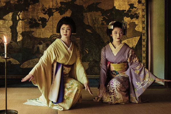 Geishas performing a ceremony in front of a gold leaf tapestry