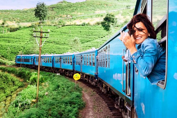 Woman leaning out of a blue train speeding through green fields
