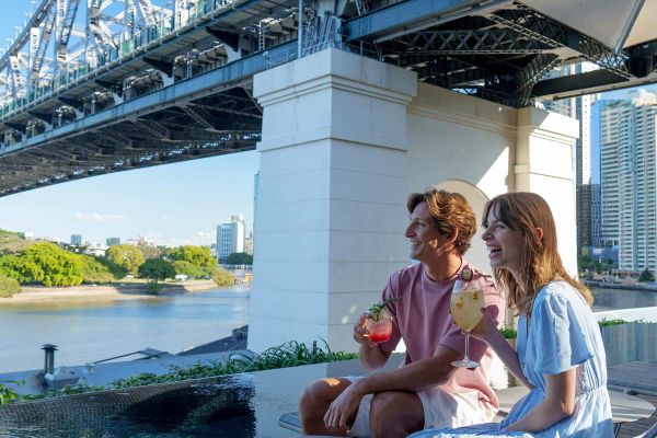 Young couple drinking cocktails sitting under Sydney Harbour Bridge