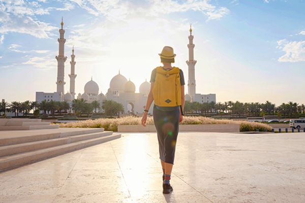 Person with yellow backpack walking away from camera towards building in abu dhabi