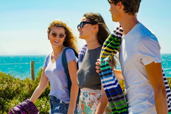 Three teenagers carrying towels on the beach